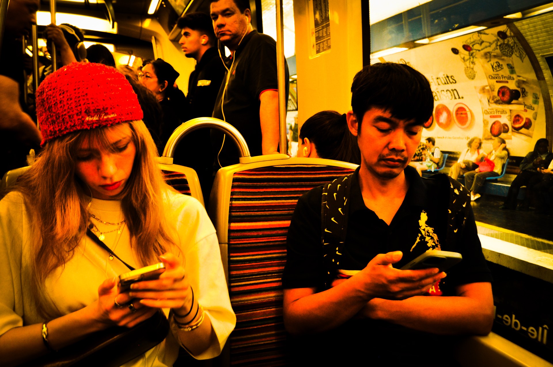 Commuters on a subway train under golden light, one in a red beanie