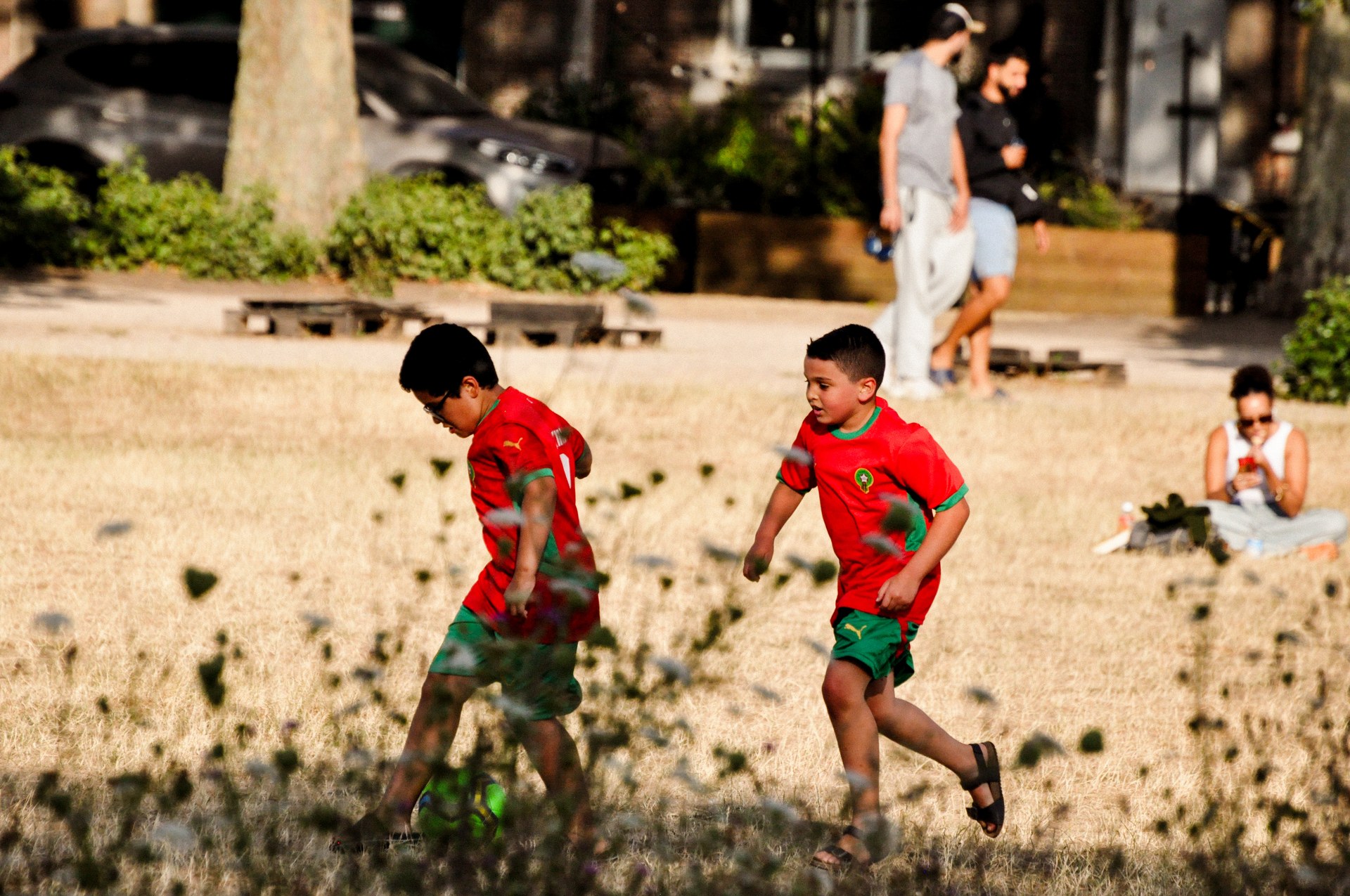 Two boys in bright jerseys chasing a ball through a sunlit park