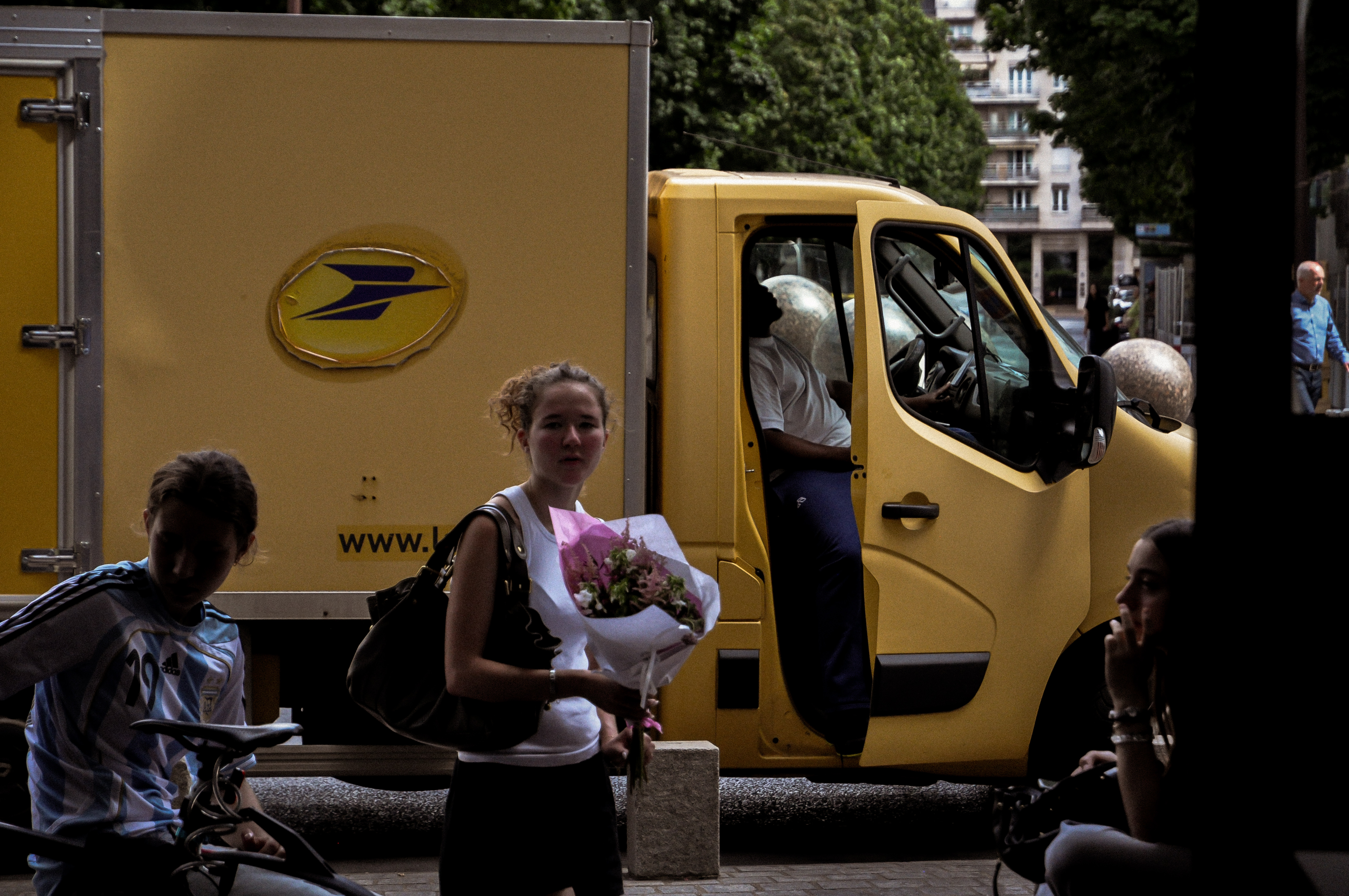 Woman with a bouquet crossing before a yellow delivery truck